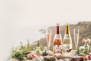 Two bottles of Wild LIfe non-alcoholic sparkling wine on a table with glasses and flowers, set against a mountainous landscape.
